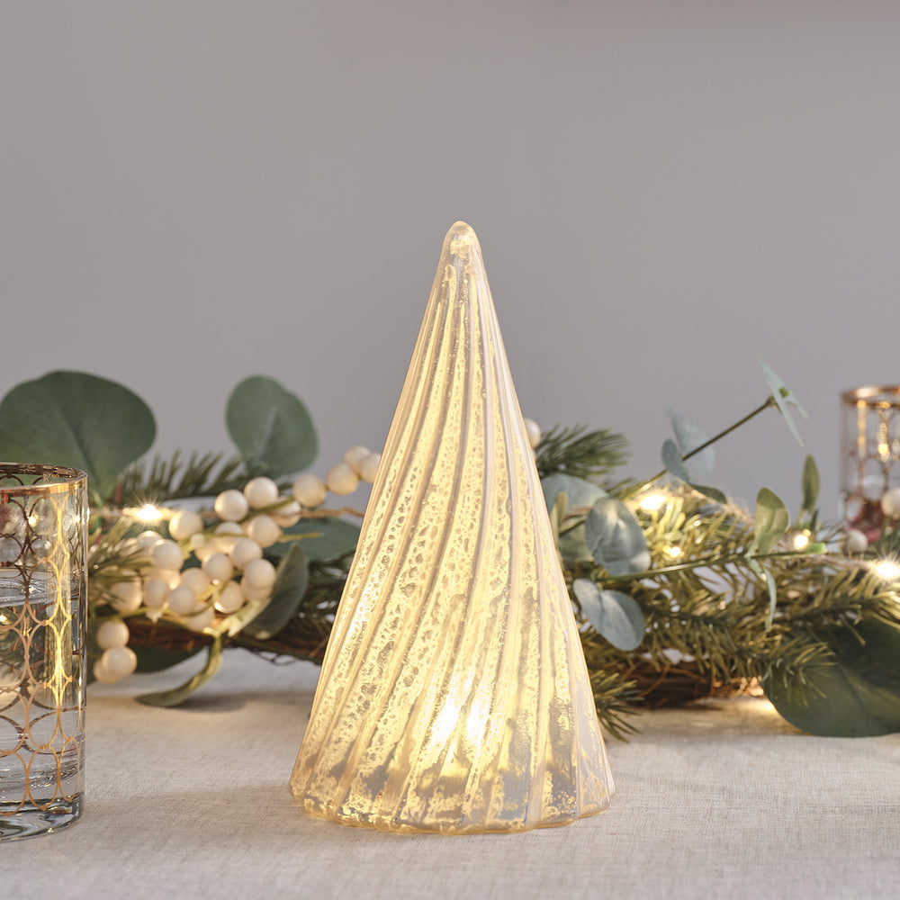 LED-Weihnachtsbaum aus Glas mit warmweißer Beleuchtung auf Tisch mit grüner Girlande und Dekoration