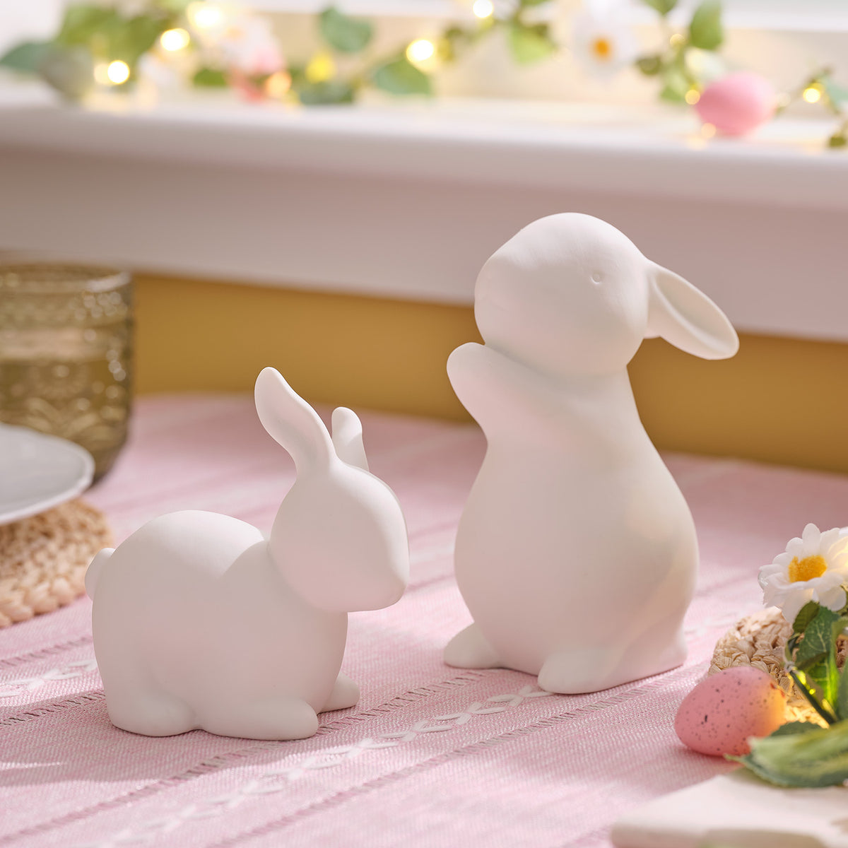Porzellan-Osterhasen mit warmweißem Licht auf rosa Tischdecke mit Osterdeko