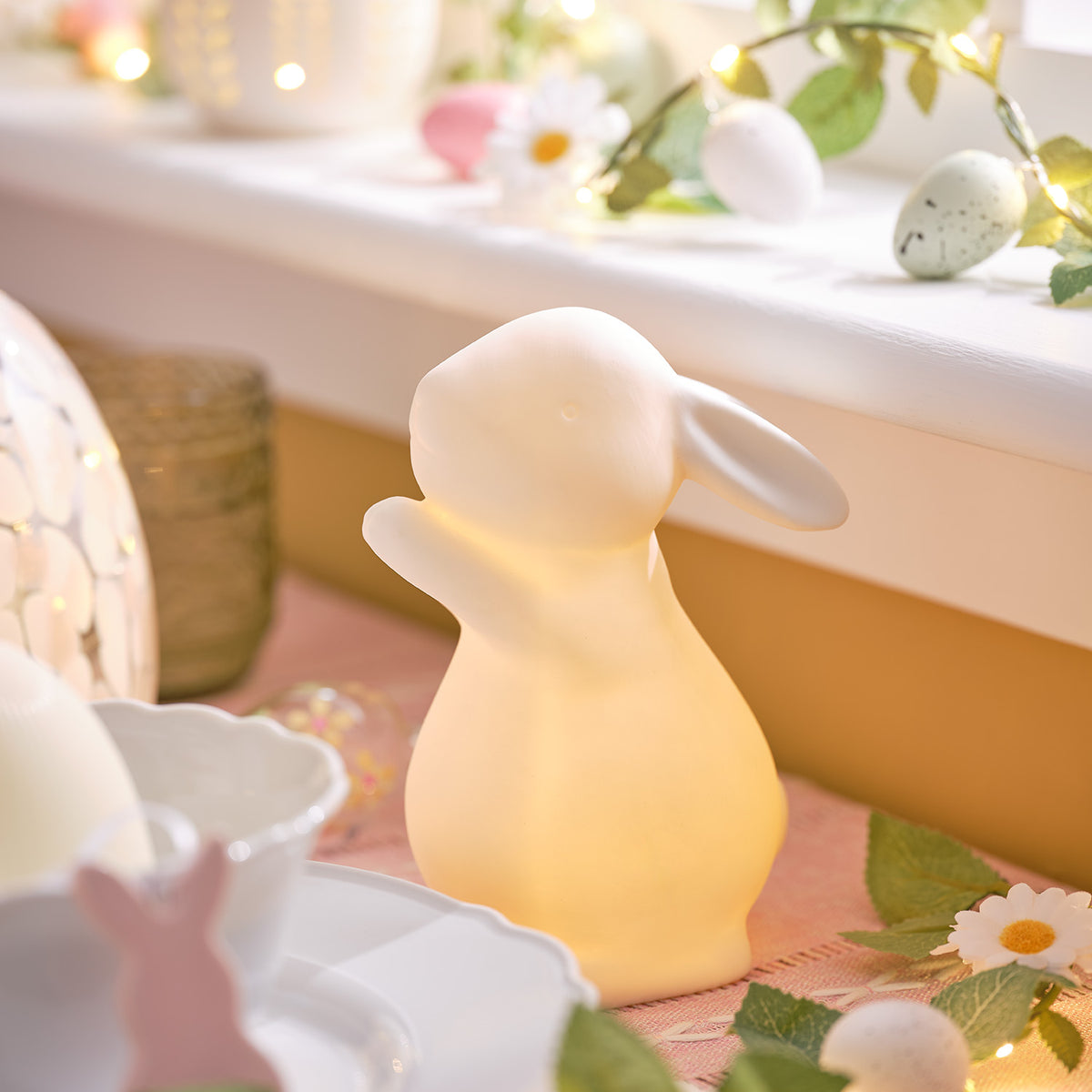 Beleuchteter Porzellan-Osterhase auf rosa Tischdecke mit Osterdeko und Eiern