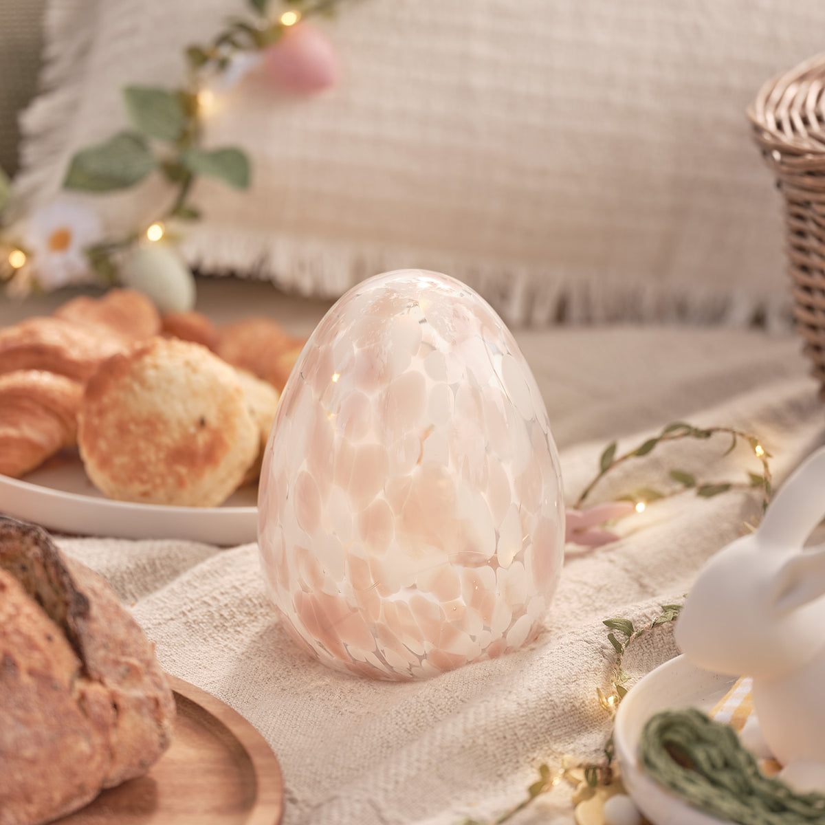 Leuchtendes Glas-Osterei mit Konfetti-Effekt auf gedecktem Frühstückstisch