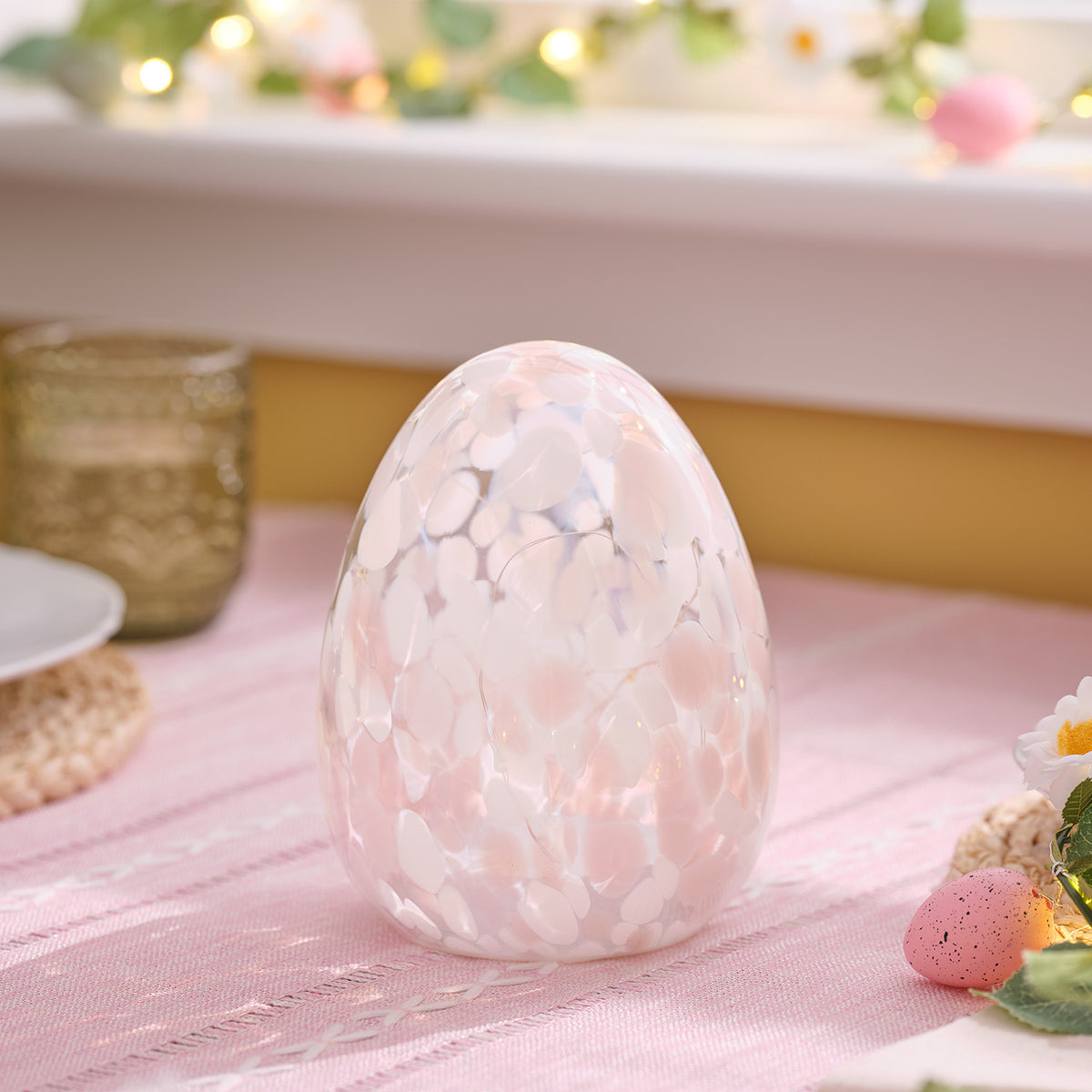 LED-Osterei aus Glas mit pastellrosa und weißen Sprenkeln auf rosa Tisch mit Deko