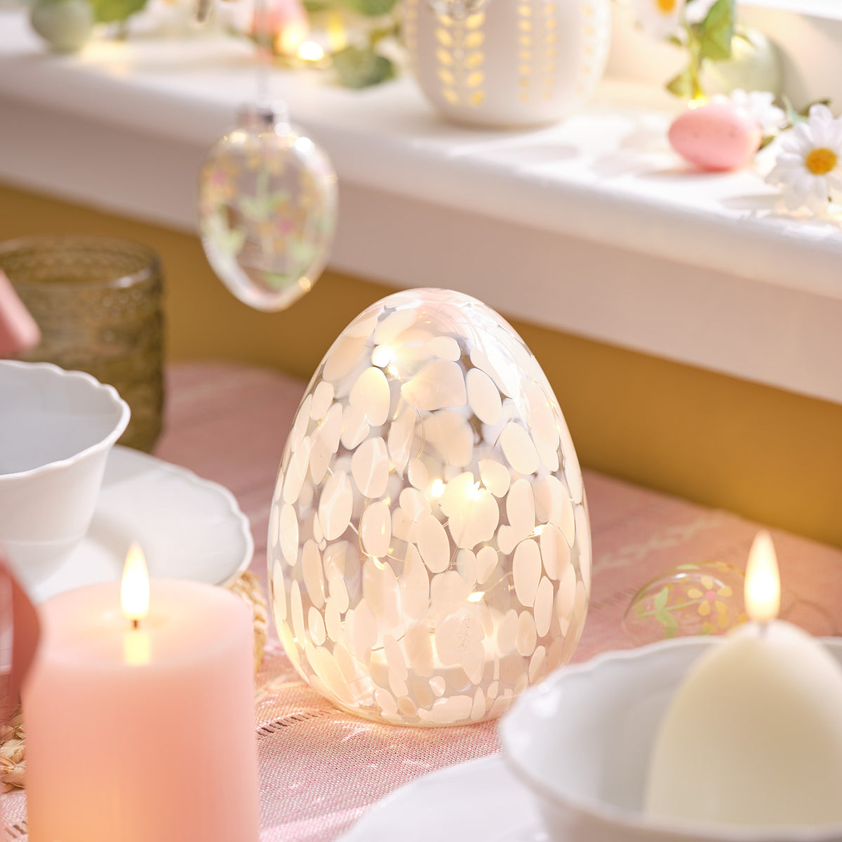 Pastellrosa LED-Osterei mit Konfetti-Muster auf gedecktem Tisch mit Kerzen