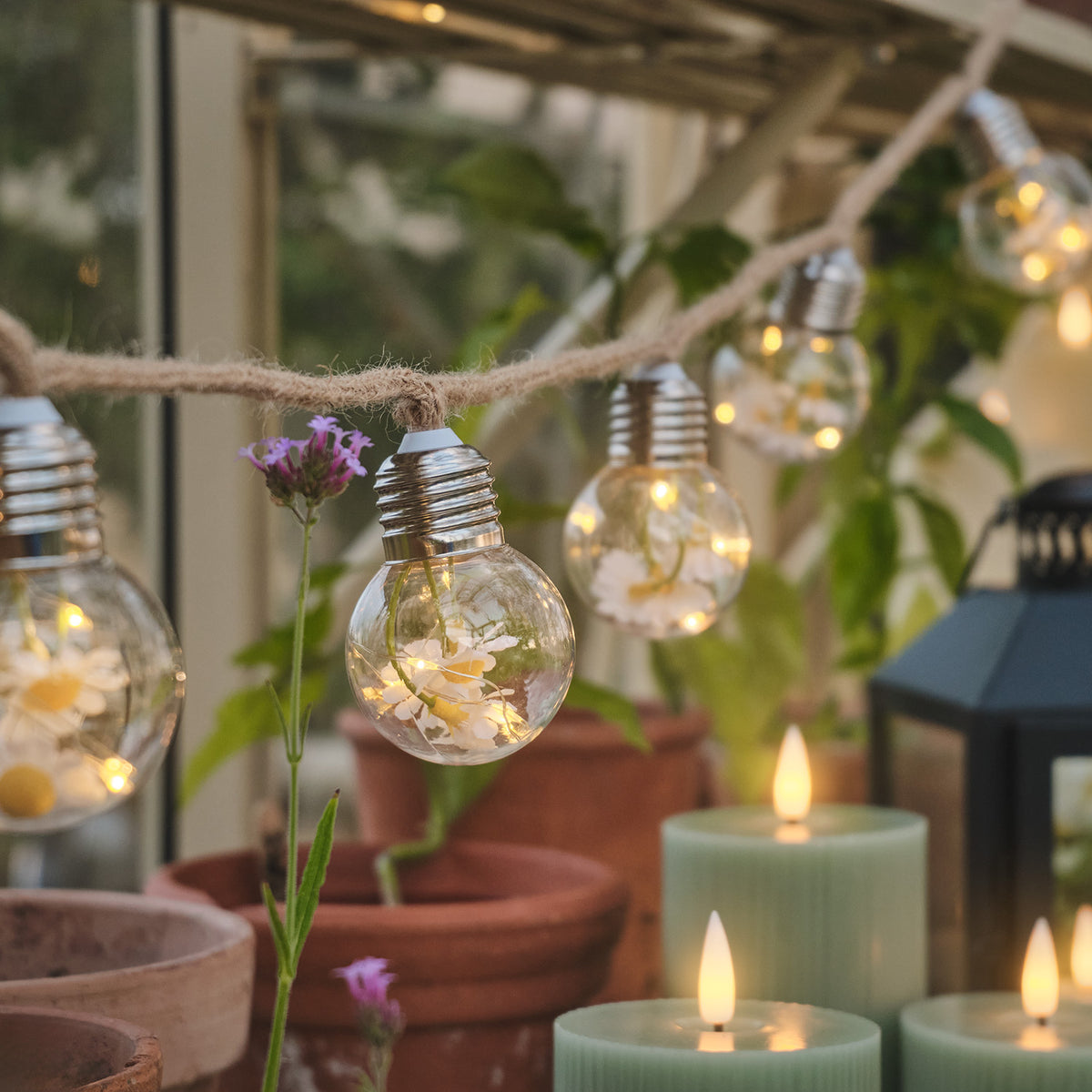 LED-Lichterkette mit klaren Glühbirnen und Gänseblümchen auf naturfarbenem Juteseil im Garten