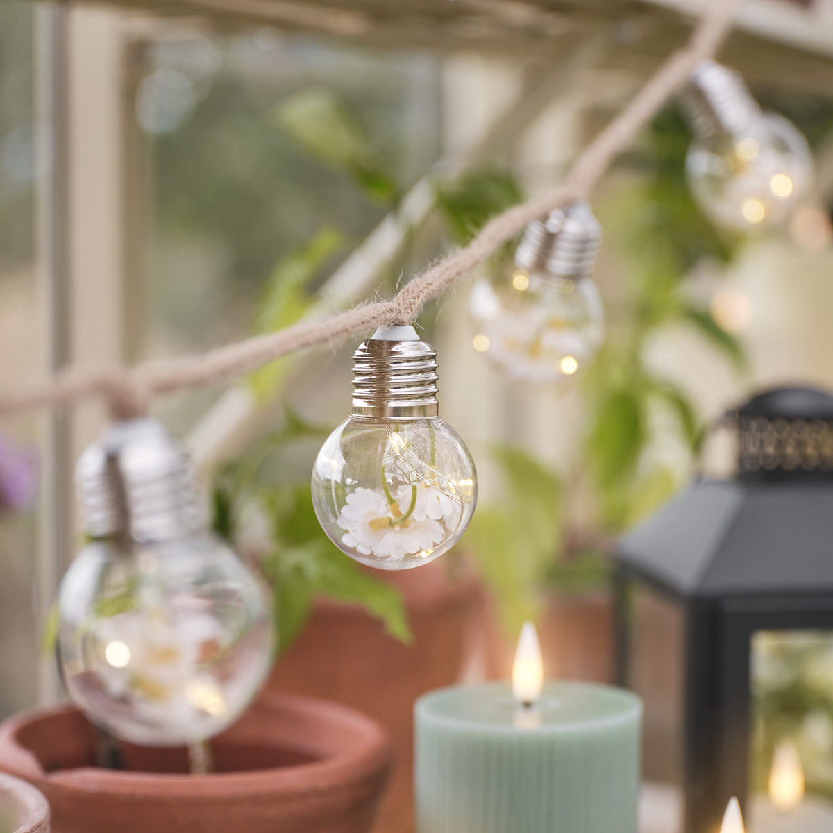 Glühbirne der LED-Lichterkette mit Gänseblümchen-Deko und warmweißem Licht vor Pflanzen