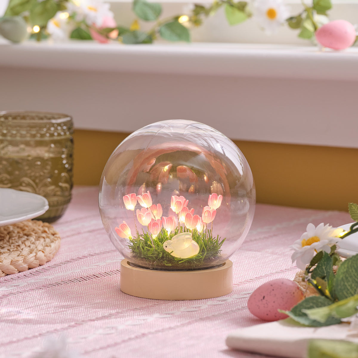 LED-Osterkugel mit warmweiß leuchtenden rosa Blumen und Hasenfigur auf künstlicher Wiese