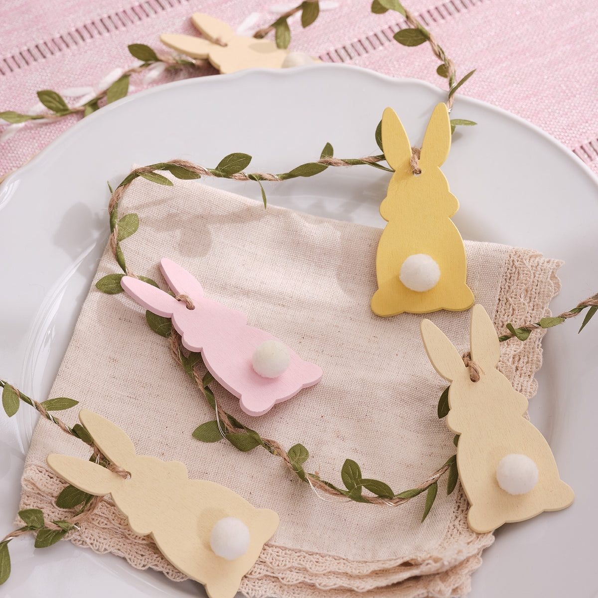 LED-Osterhasen-Girlande mit zehn Holzhasen in Rosa, Gelb und Buttergelb auf einem weißen Teller
