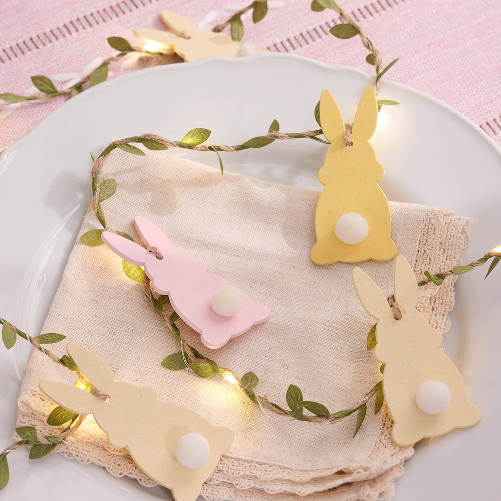 Pastellfarbene Holzhasen mit Puschelschwänzchen und warmweißen LED-Lichtern auf Juteband