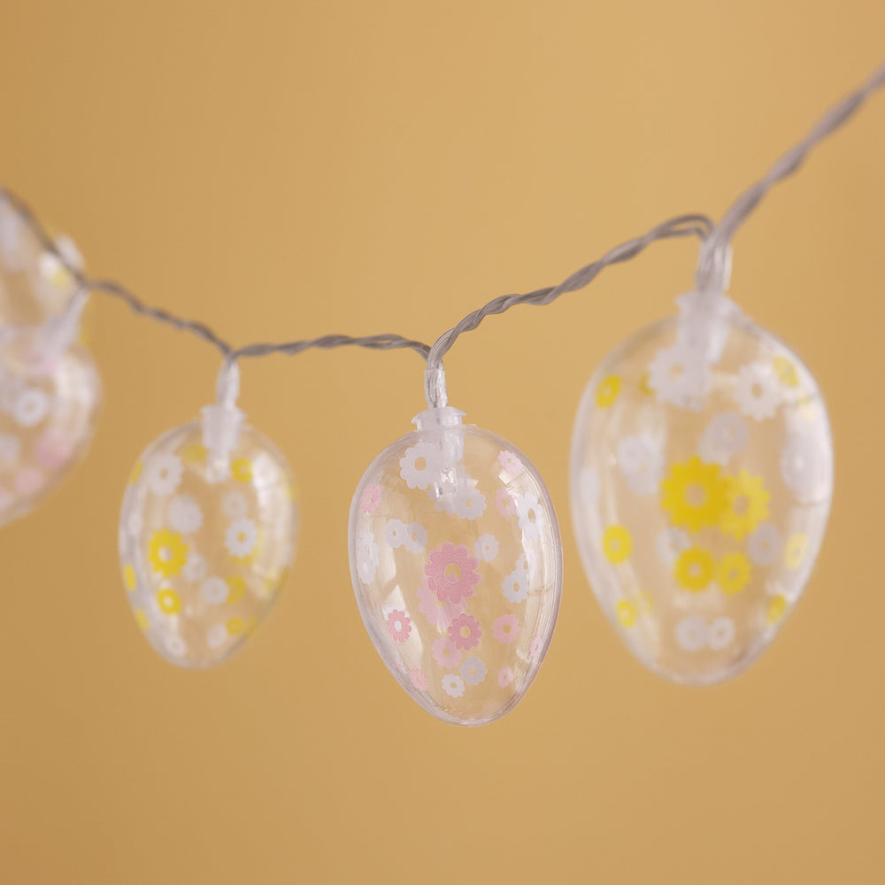 Transparente Ostereier mit rosa und gelben Blumen auf einer unbeleuchteten LED-Lichterkette