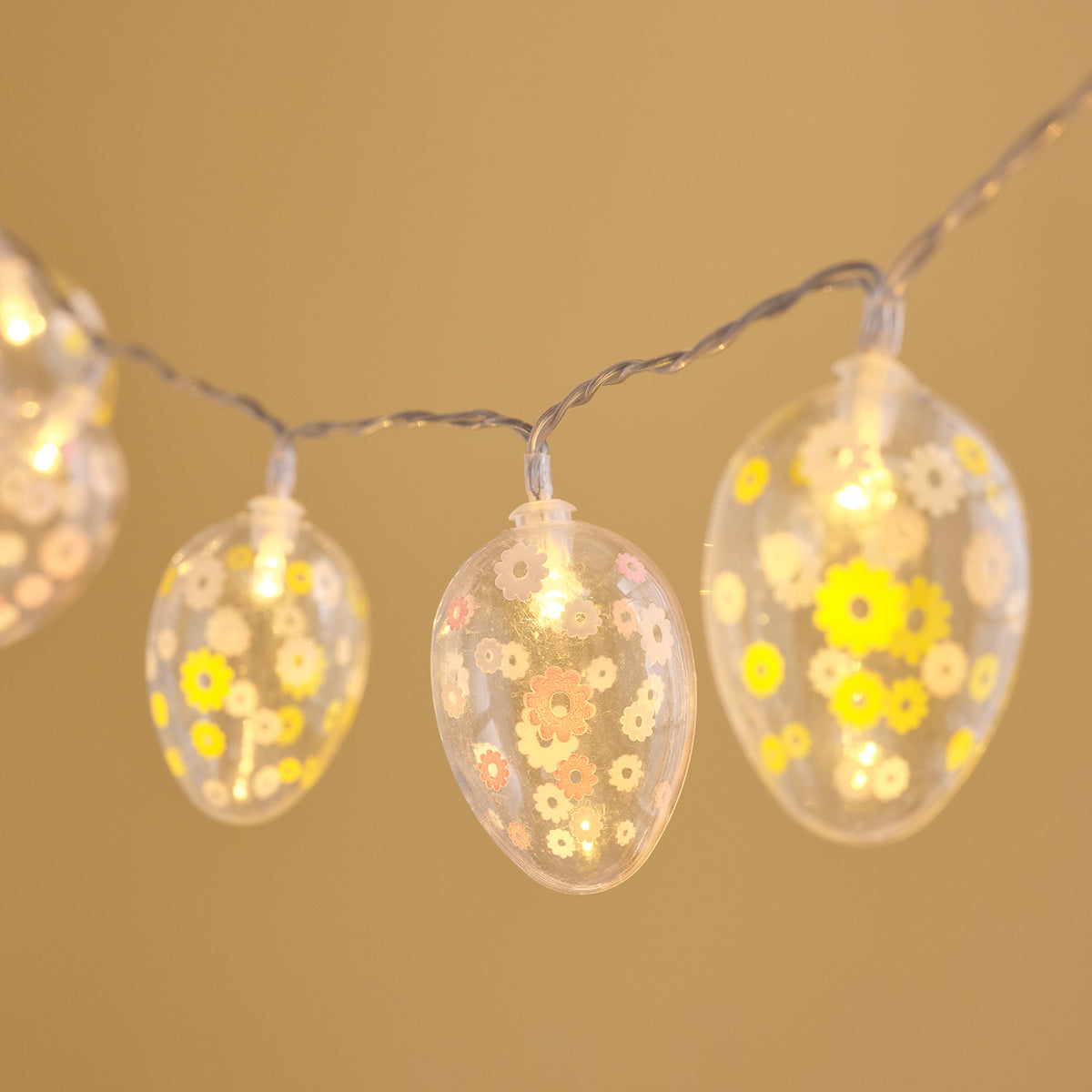 Nahaufnahme von leuchtenden transparenten Ostereiern mit gelben und weißen Blumen auf Lichterkette