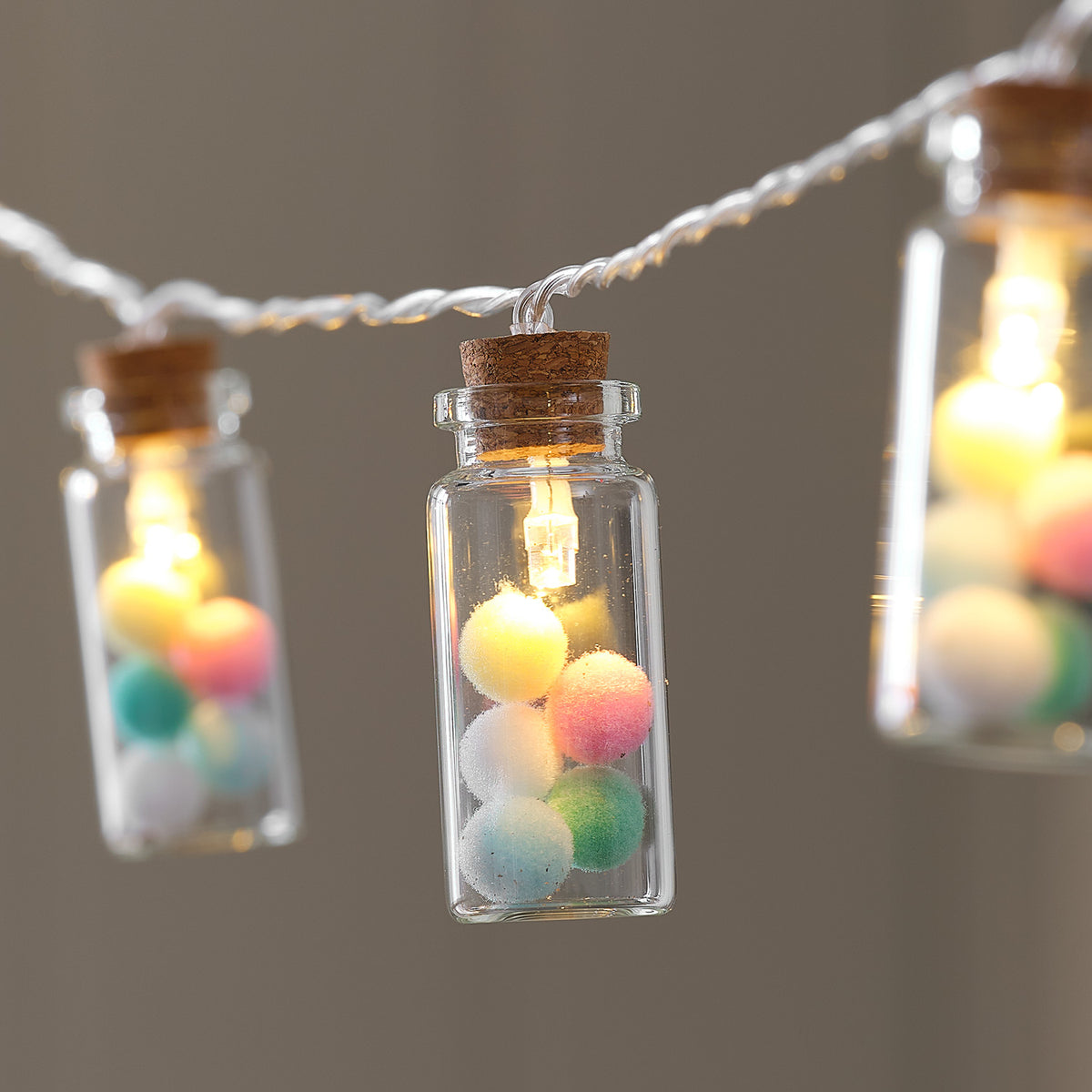 Nahaufnahme eines Glasfläschchens mit bunten Pastell-Pompoms und warmweiß leuchtender LED