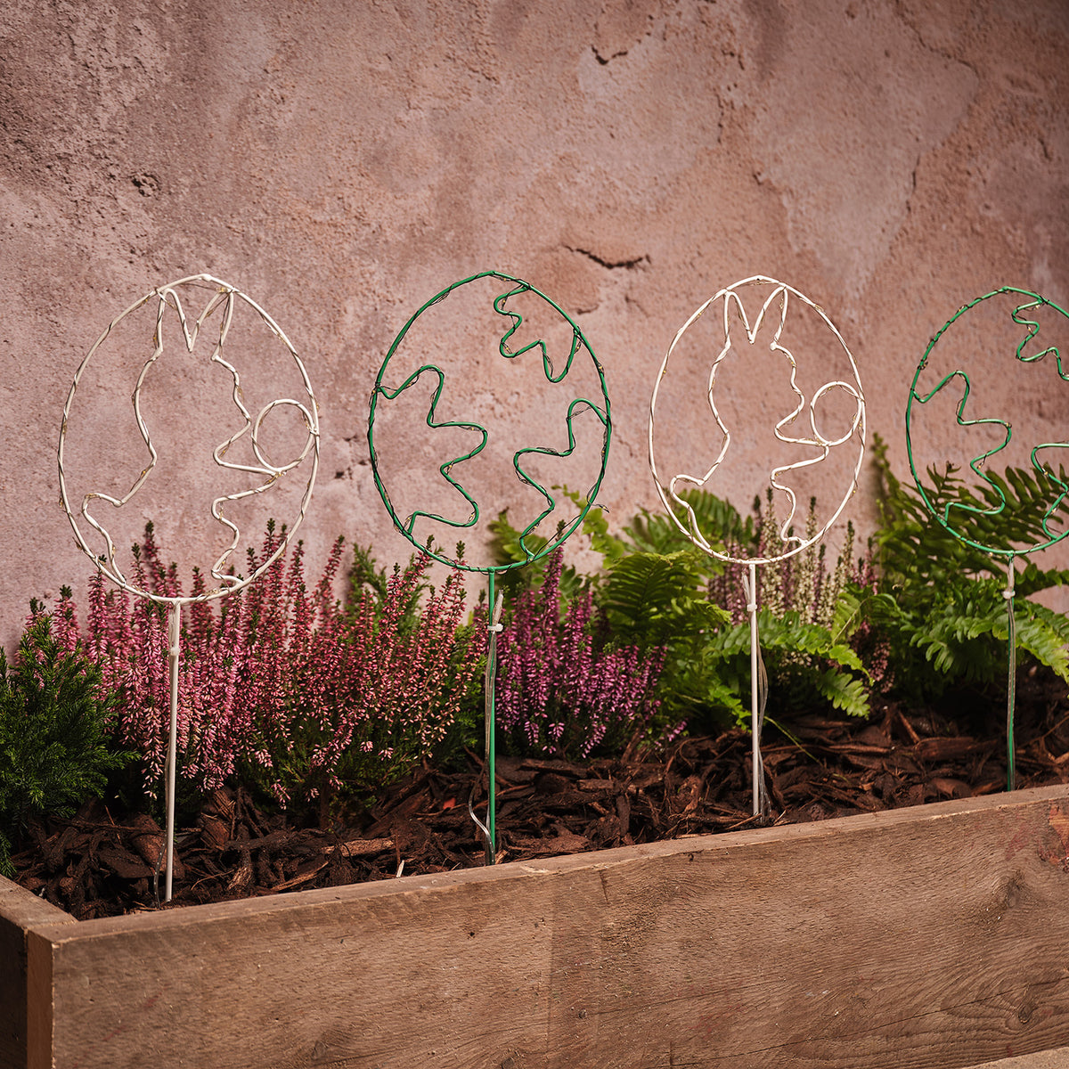 Vier beleuchtete LED-Osterei-Gartenstecker mit Hasen- und Blumenmotiven im Beet