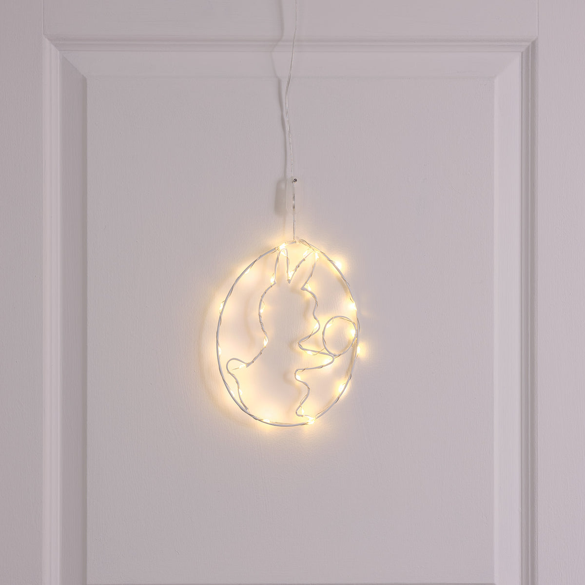 LED-Osterei mit Häschen-Motiv und warmweißen Mikro-LEDs an weißer Tür hängend