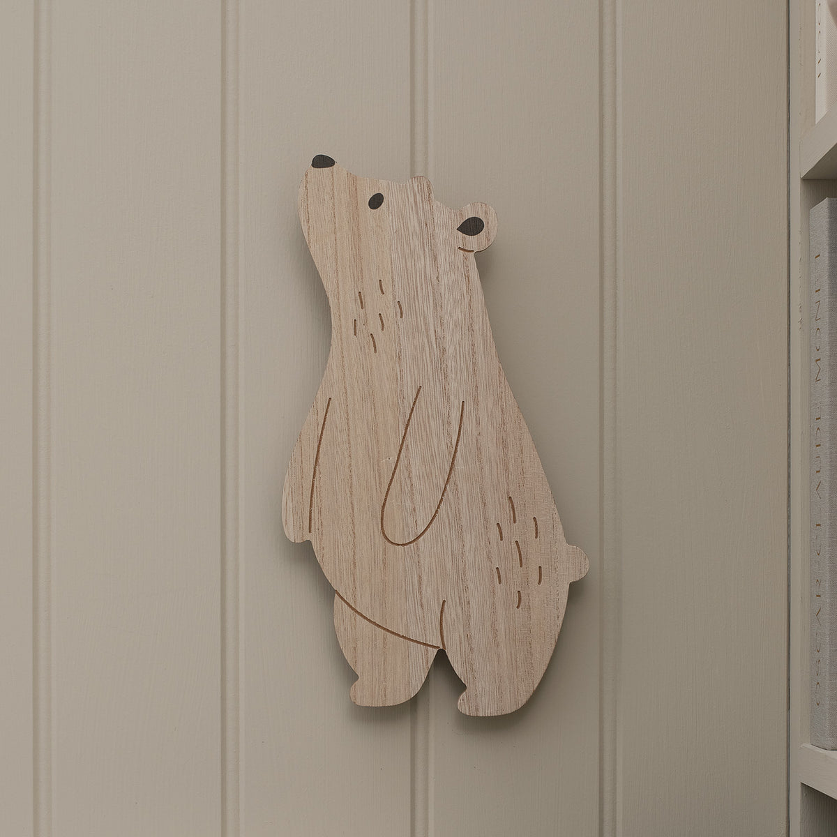Holz-Wandlampe in Bärform ohne Licht an weißer Wand neben Regal mit Büchern