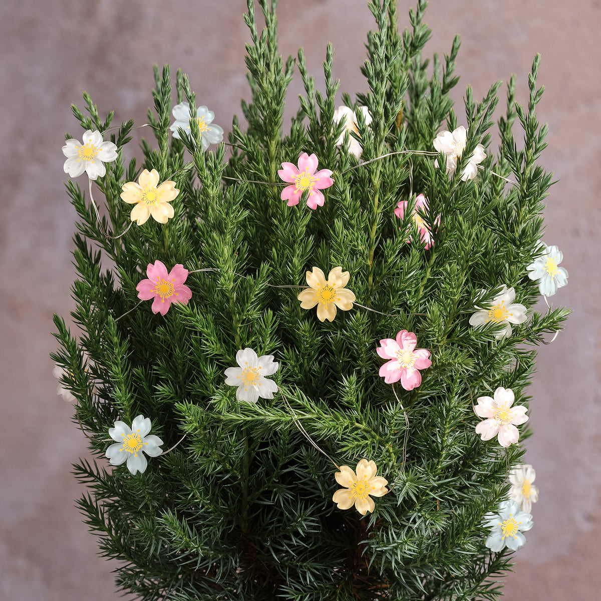Pastellfarbene Blumenlichterkette dekorativ in grünen Zweigen drapiert