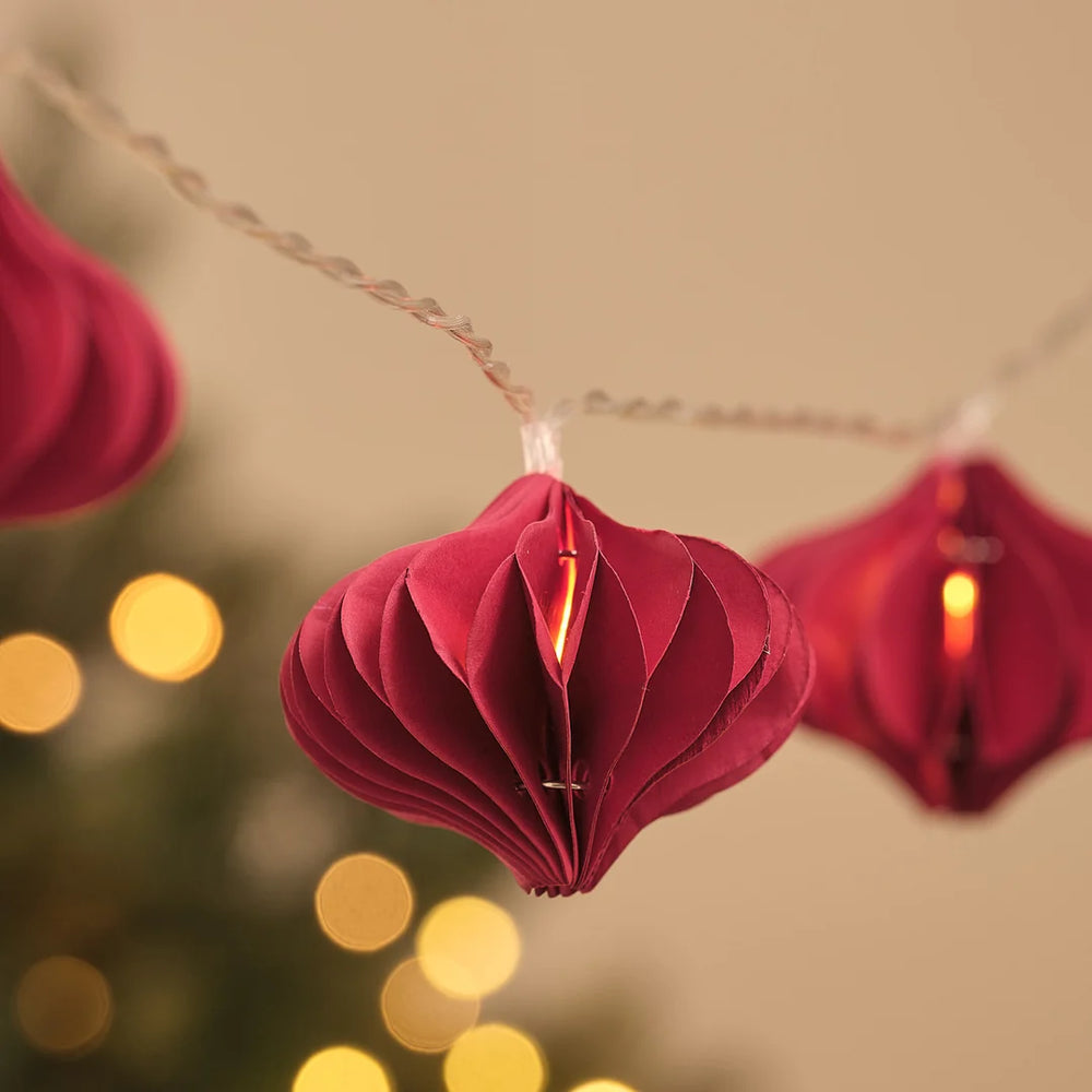 Detailansicht roter Papier-Weihnachtsanhänger an Lichterkette vor Lichterglanz.