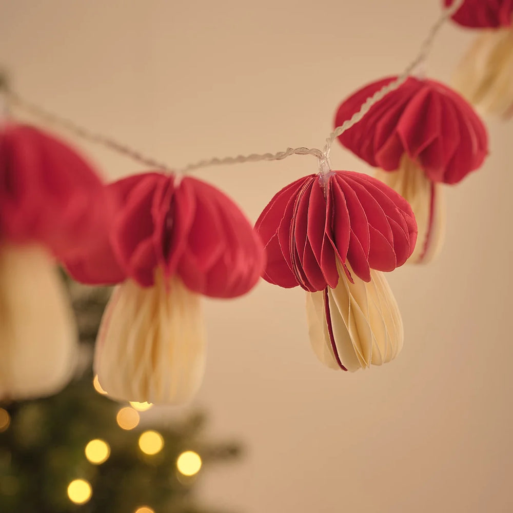 Lichterkette mit mehreren roten Papier-Pilz-Anhängern vor Lichterglanz.
