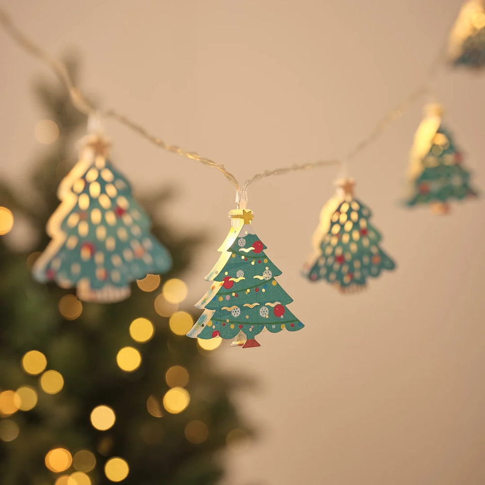 Lichterkette mit Tannenbaum-Anhängern mit Sternspitze vor Weihnachtsbaum und Lichterglanz.