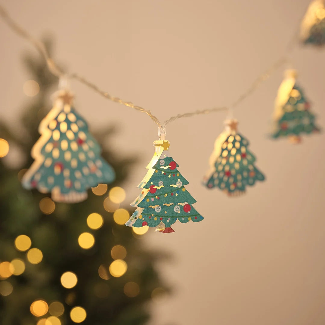 Lichterkette mit Tannenbaum-Anhängern mit Sternspitze vor Weihnachtsbaum und Lichterglanz.