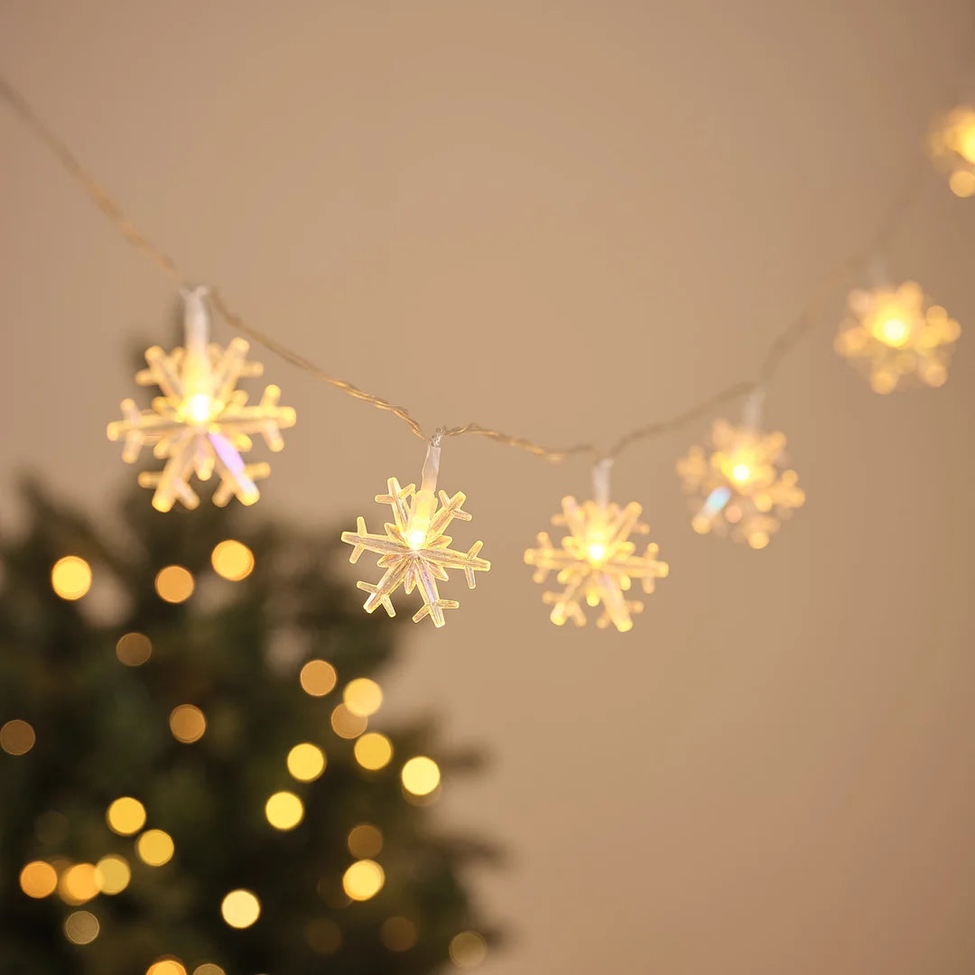 LED-Lichterkette mit leuchtenden Schneeflocken-Anhängern vor Weihnachtsbaum und Lichterglanz.