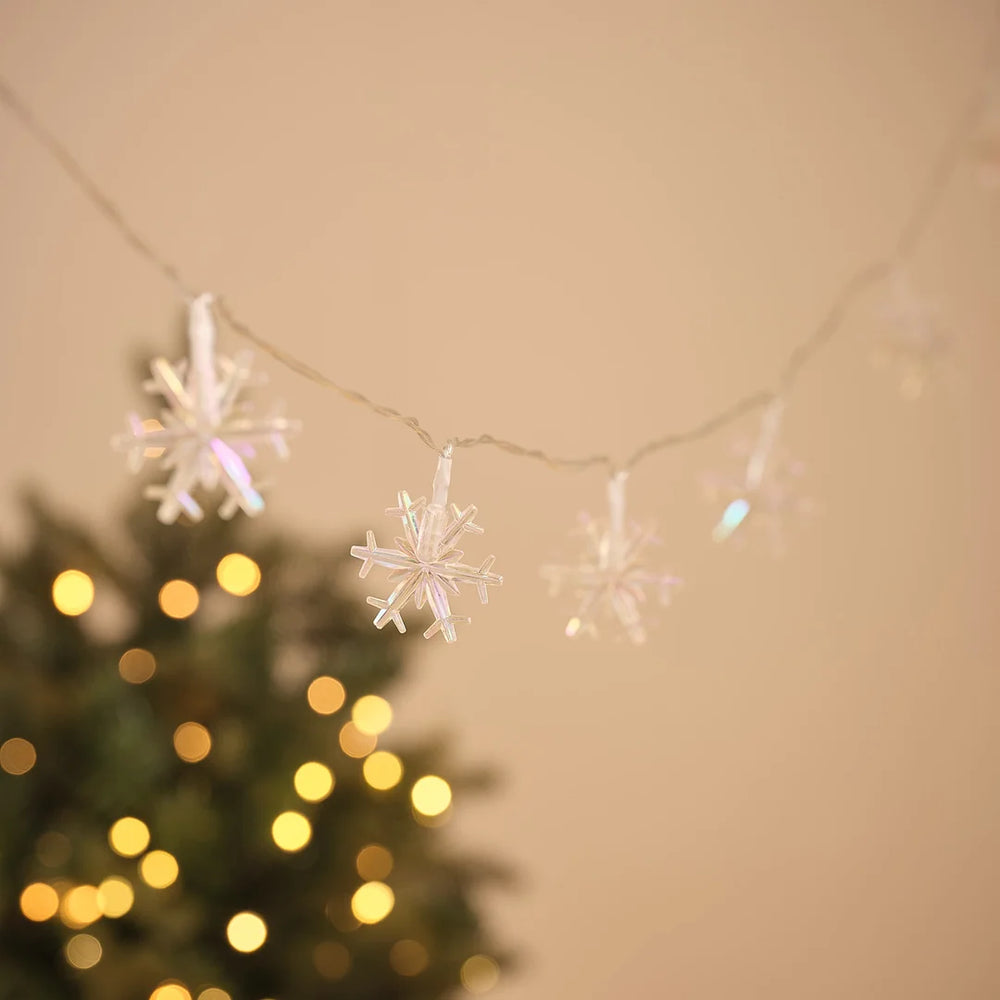 LED-Lichterkette mit mehreren Schneeflocken-Anhängern vor Tannengrün.