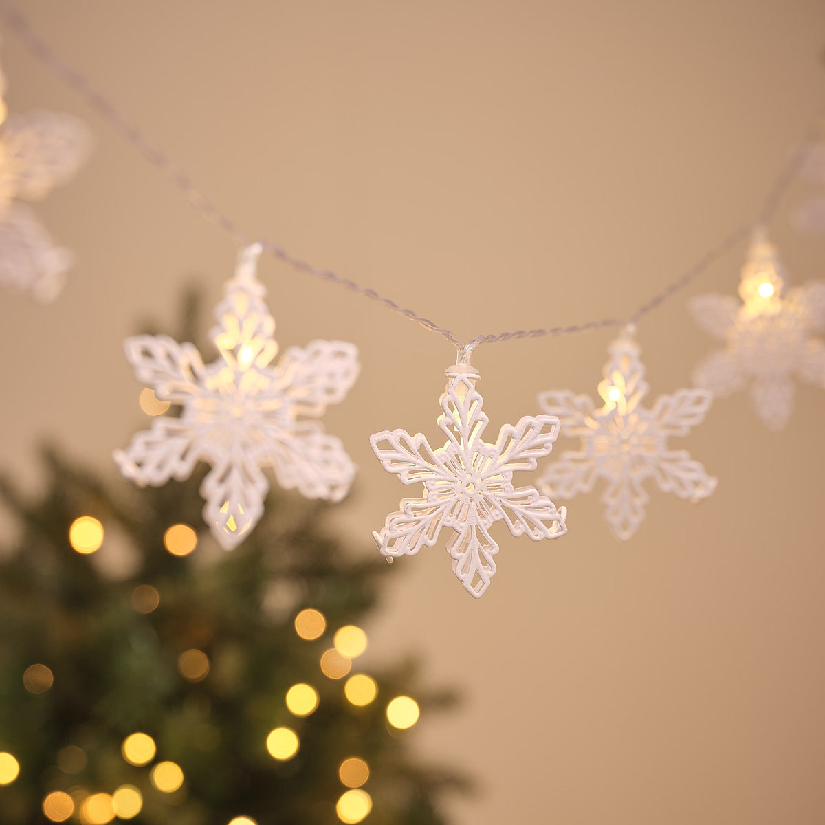 LED-Lichterkette mit 20 warmweißen Metall-Schneeflocken vor unscharfem Weihnachtsbaum