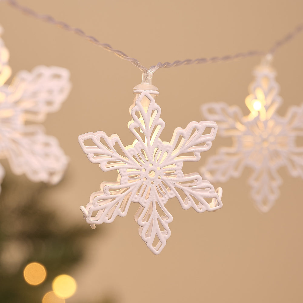 Nahaufnahme einer beleuchteten weißen Metall-Schneeflocke an transparenter LED-Lichterkette