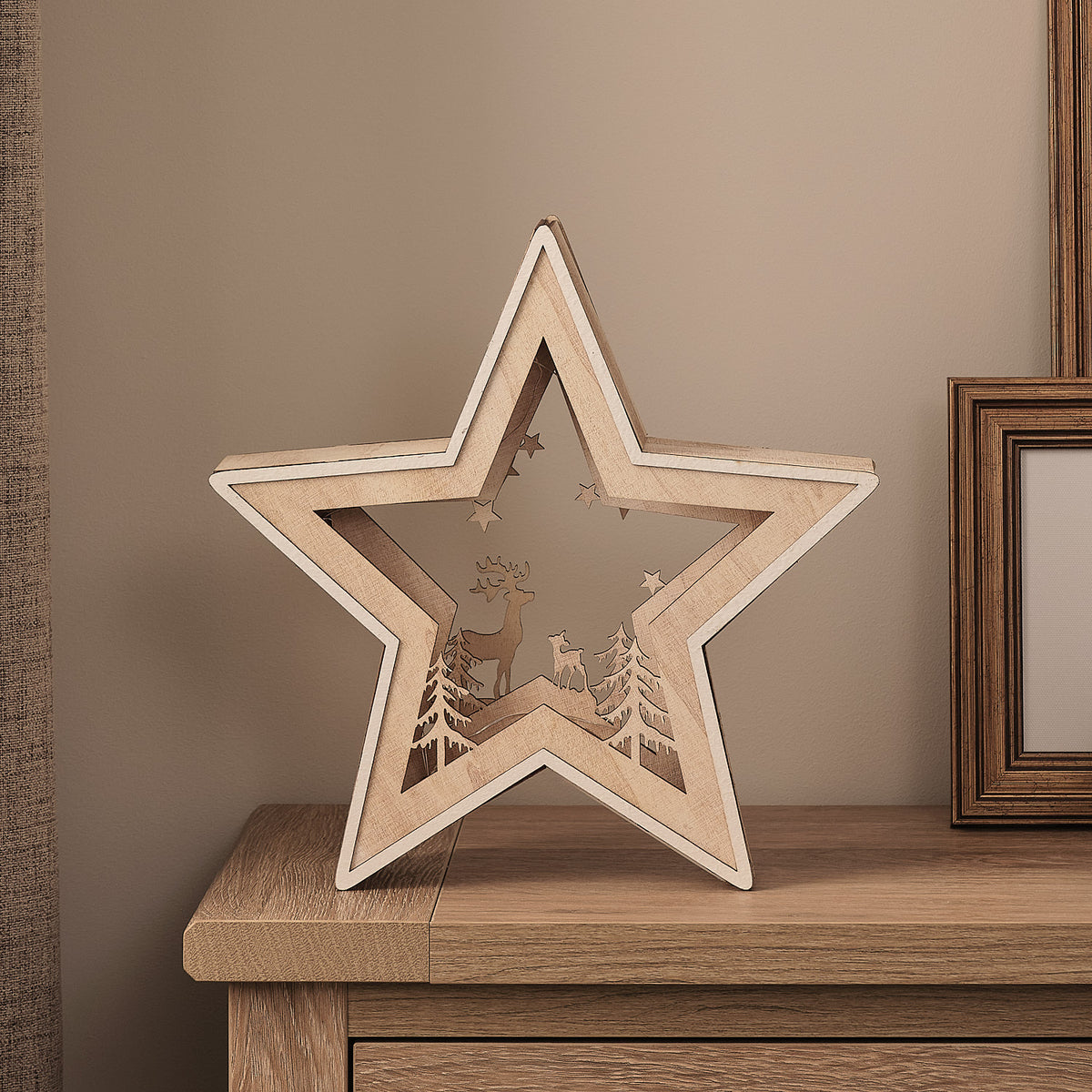 Unbeleuchtete Holzstern-Silhouette mit Rentier und Tannenbäumen auf Holzkommode vor Wand