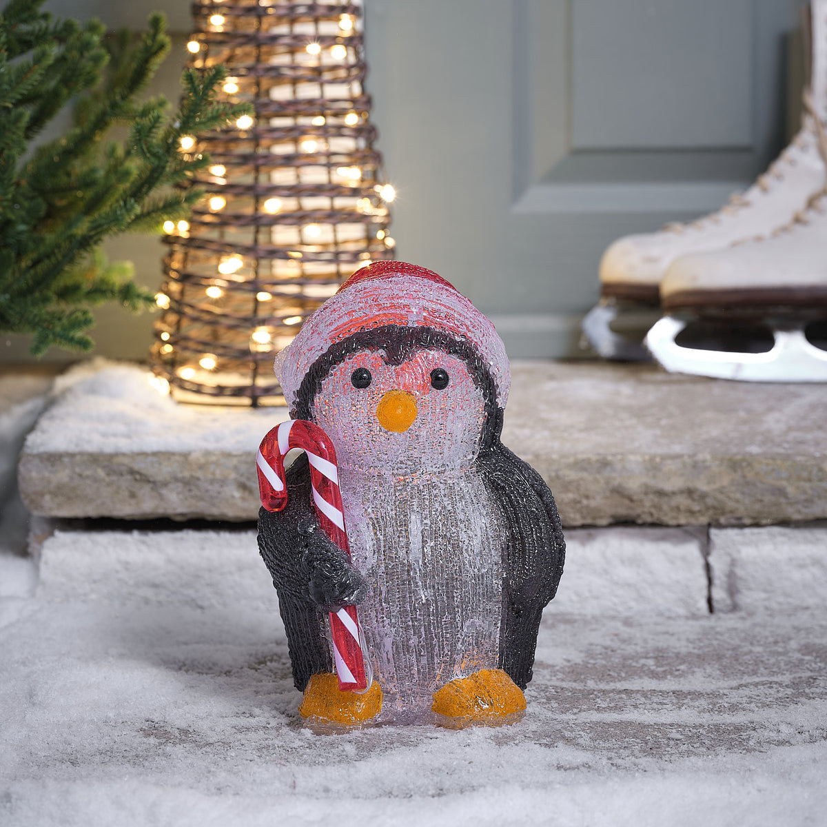 LED-Acryl-Pinguin mit roter Weihnachtsmütze und Zuckerstange auf verschneitem Boden