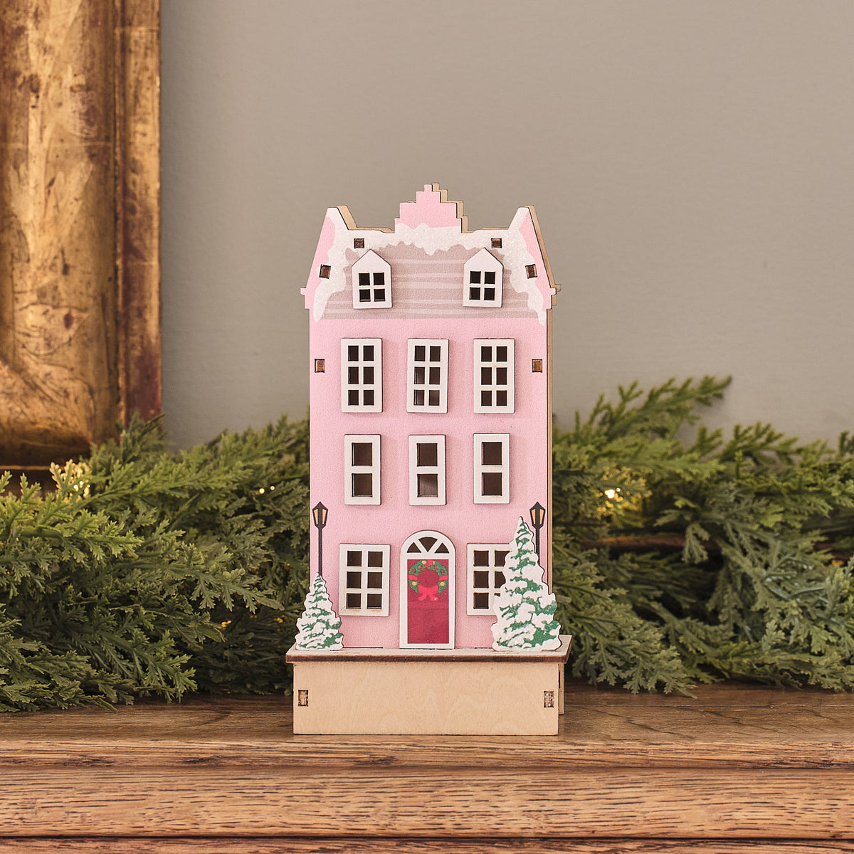 LED-Holzhaus in Rosa ohne Beleuchtung mit sichtbaren Fenstern und winterlichen Tannenbäumen