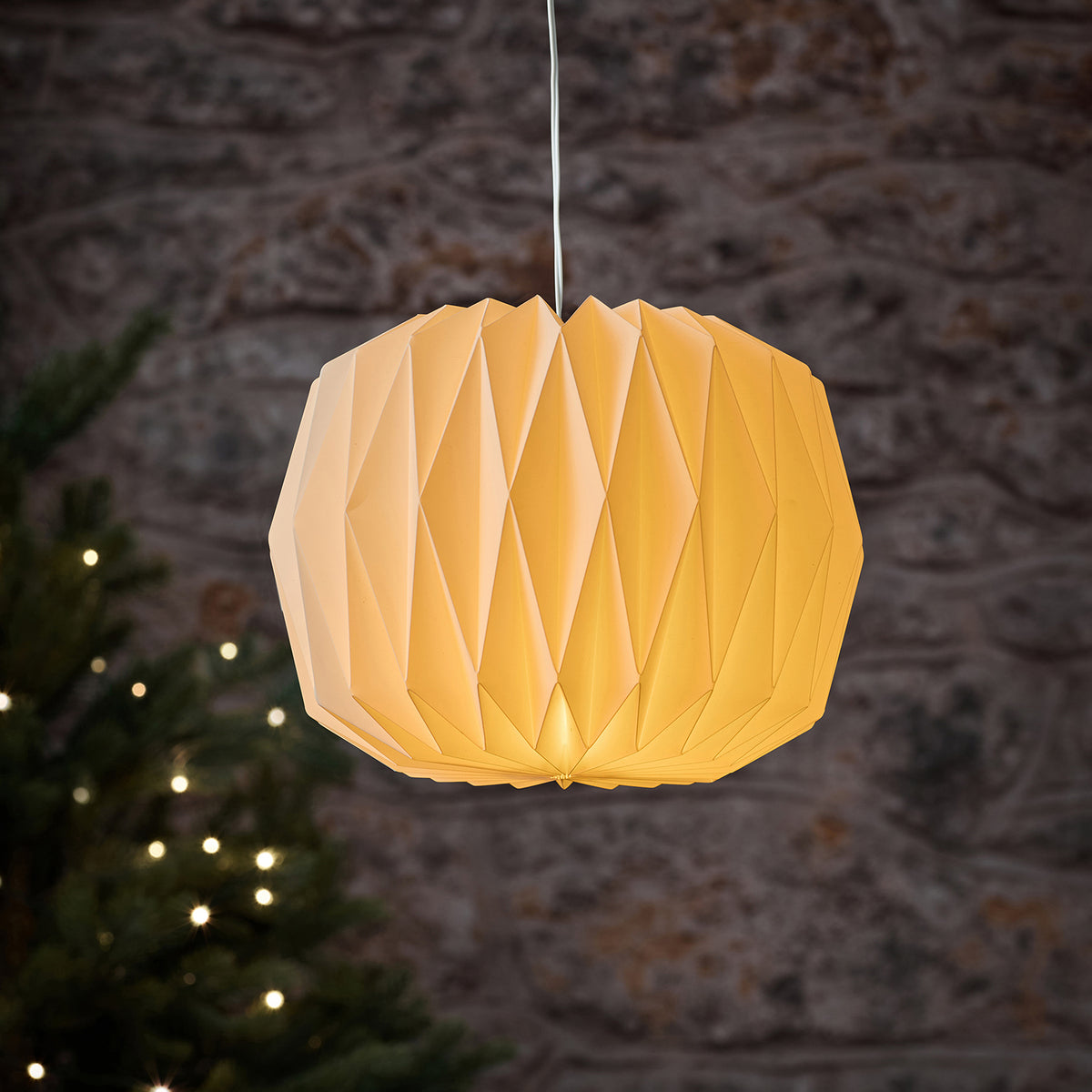 Nahaufnahme weiße LED-Papierlaterne mit warmweißem Licht vor Steinwand mit Weihnachtsbeleuchtung
