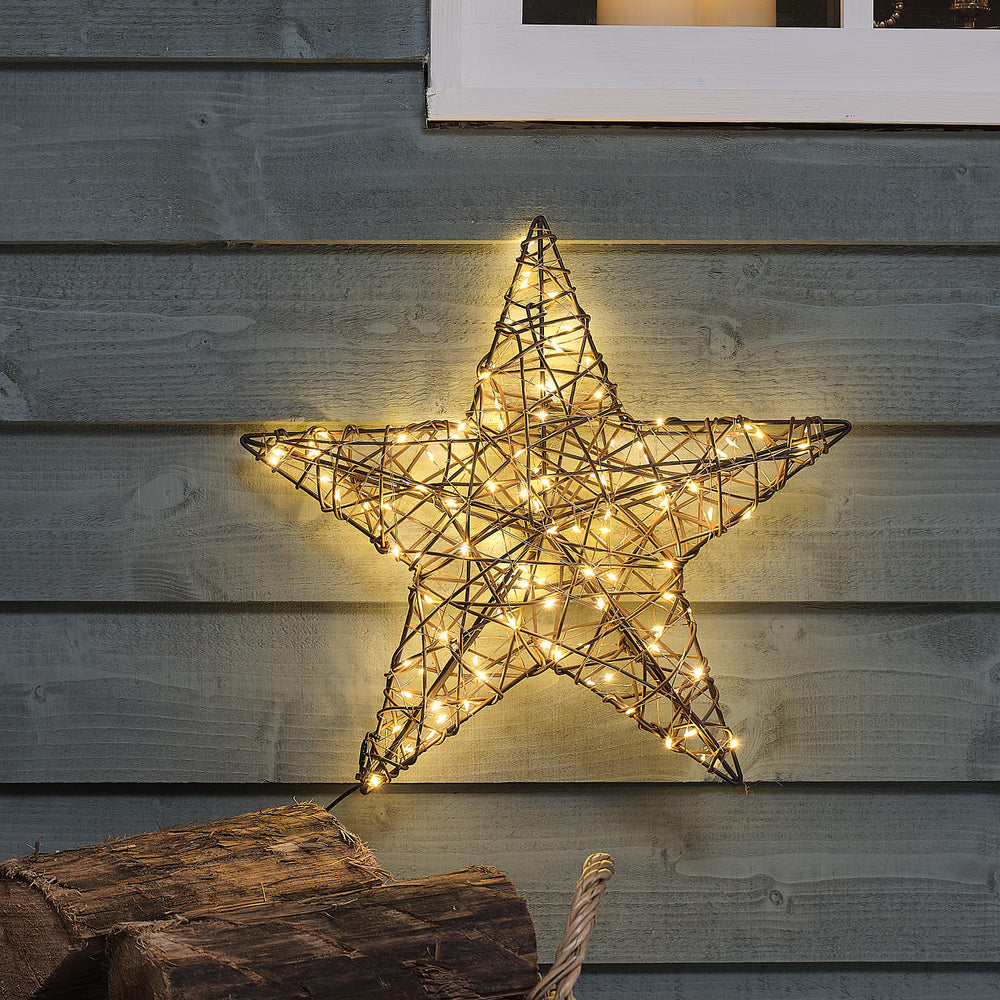 Leuchtender Rattanstern mit warmweißen LEDs an grauer Holzfassade bei Dämmerung