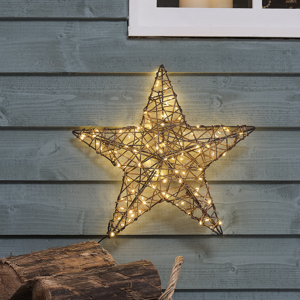 Nahaufnahme eines LED-Rattansterns mit warmweißem Licht an grauer Holzfassade