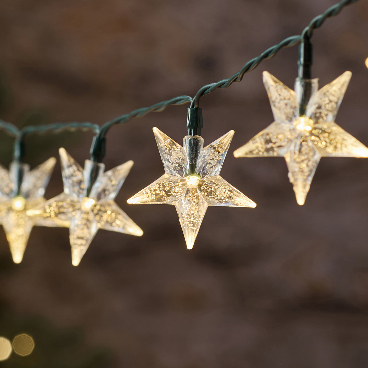 Nahaufnahme eines warmweiß leuchtenden Sterns der LED-Lichterkette mit grünem Kabel