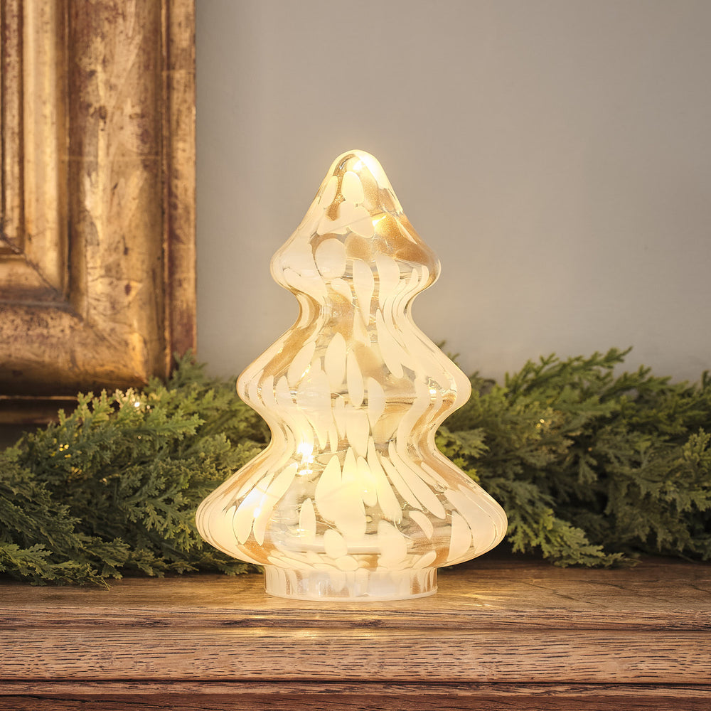 Champagnerfarbener LED-Weihnachtsbaum aus Konfetti-Glas auf Holzfläche mit Tannengrün im Hintergrund
