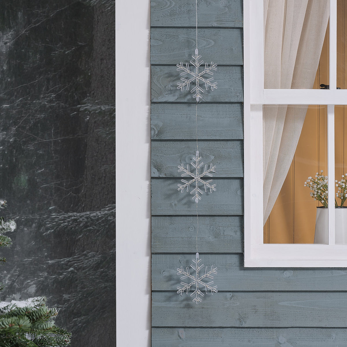 Drei unbeleuchtete transparente Acryl-Schneeflocken hängen an einer Holzfassade neben einem Fenster