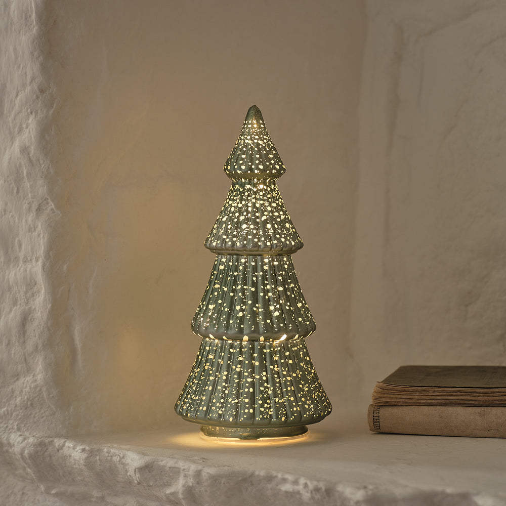 Nahaufnahme grüner LED Tannenbaum aus Glas mit goldenen Sprenkeln vor weißer Wand
