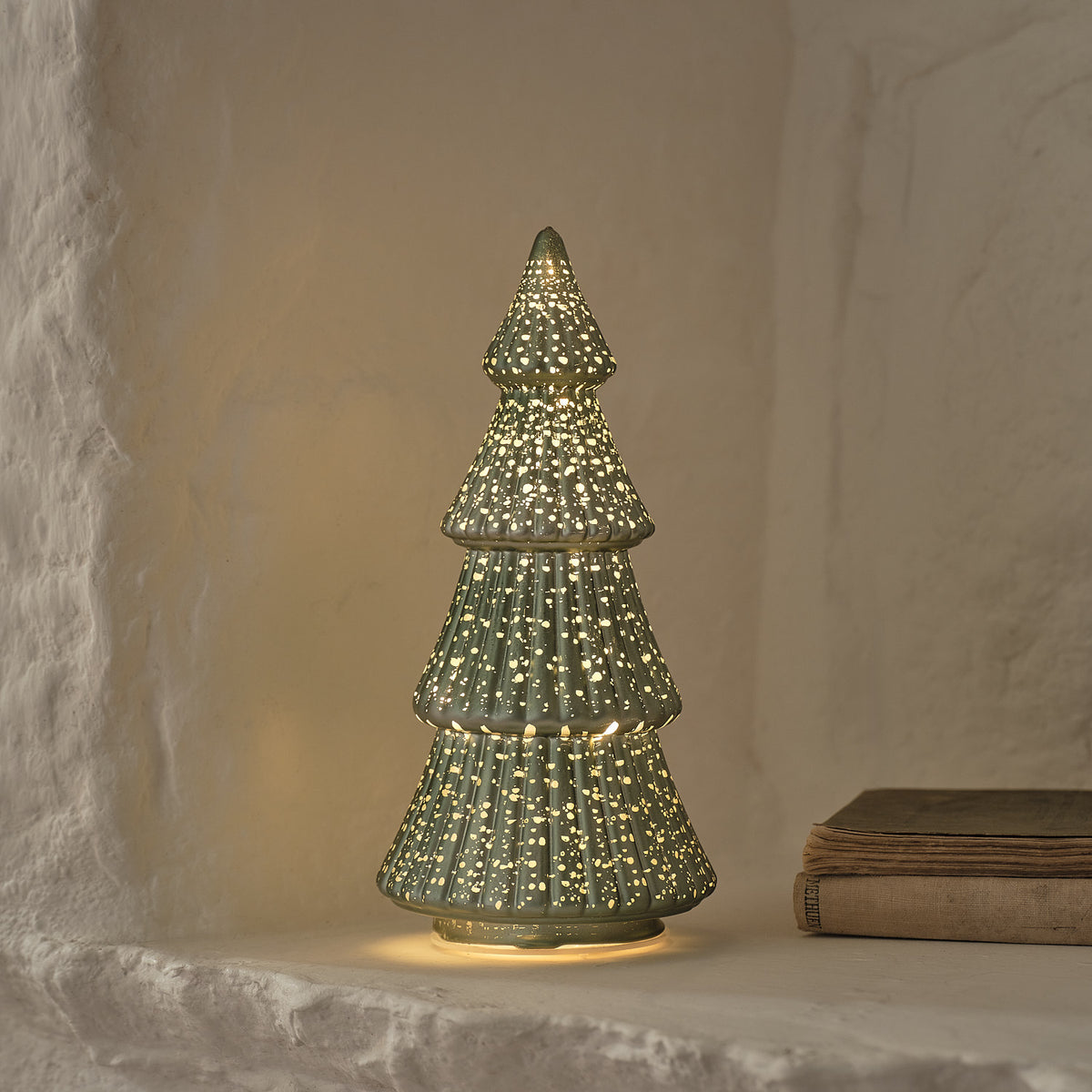 Nahaufnahme grüner LED Tannenbaum aus Glas mit goldenen Sprenkeln vor weißer Wand