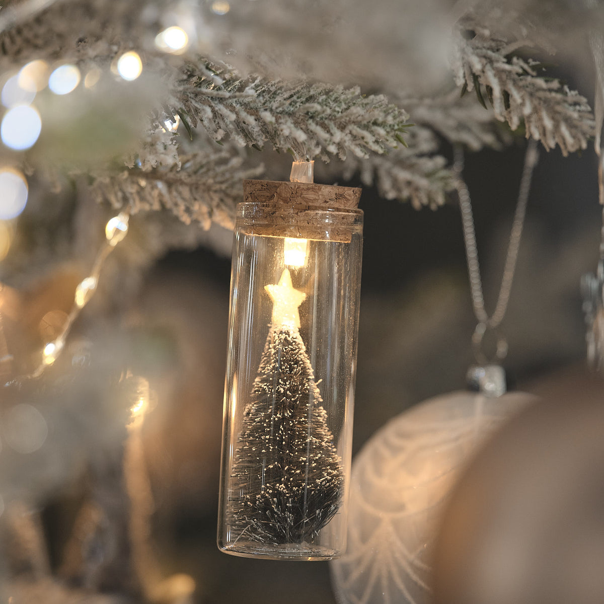 Nahaufnahme einer Glasflasche mit beleuchtetem Tannenbaum und goldenem Stern im Korkverschluss