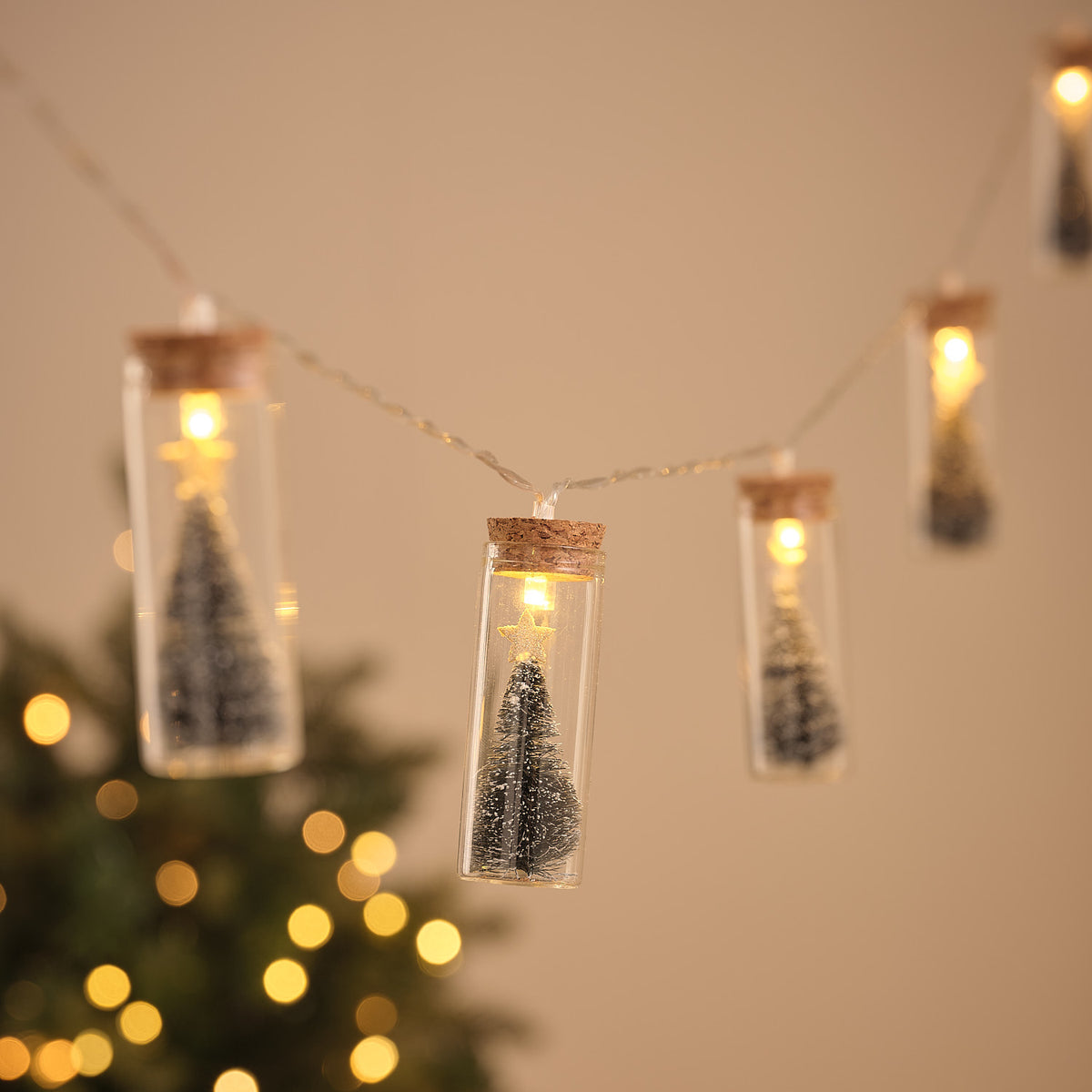 LED-Lichterkette mit Glasflaschen, jede mit schneebedecktem Tannenbaum und warmweißem Licht