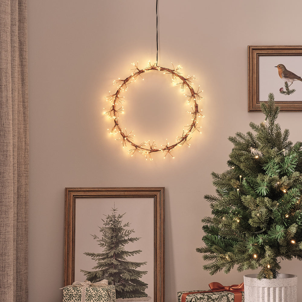 Goldener Starburst LED-Lichterkranz mit warmweißen Mikro-LEDs an Wand über Weihnachtsbaum