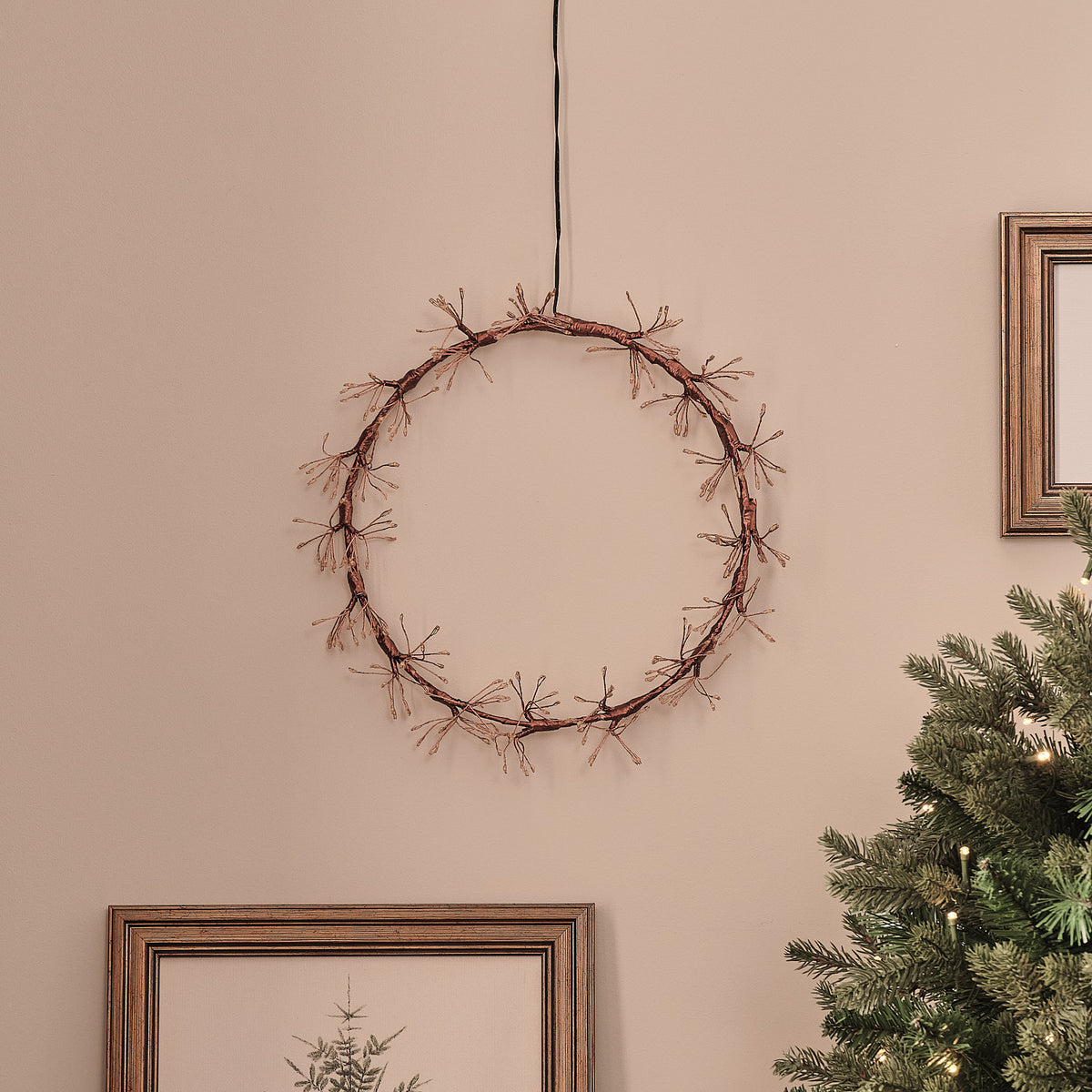 Goldener LED-Lichterkranz ohne Beleuchtung an Wand über Weihnachtsbaum und Bilderrahmen