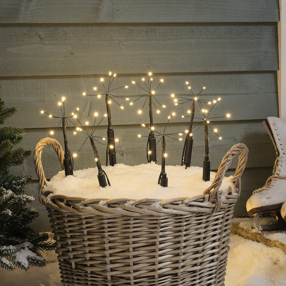 Zehn LED-Gartenstecker mit warmweißen Mikro-LEDs in einem Korb mit Kunstschnee vor Holzwand