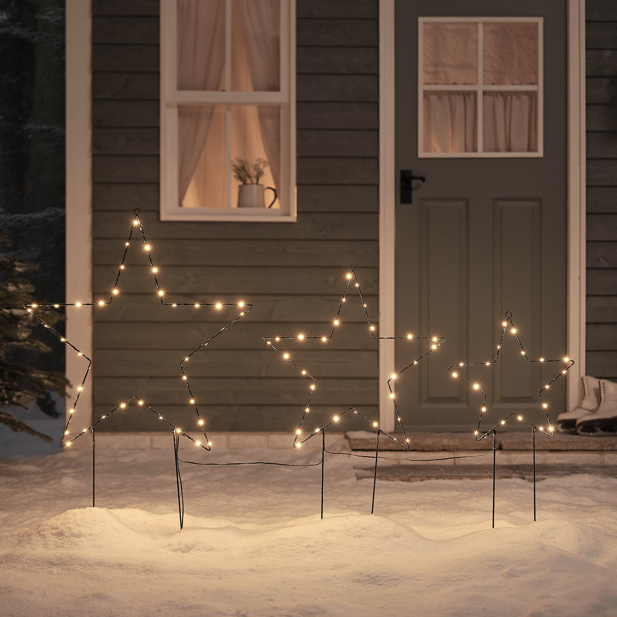 Drei schwarze LED-Stern-Gartenstecker mit warmweißen Mikro-LEDs im Schnee vor Haustür