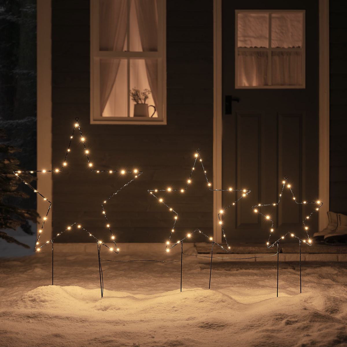 Beleuchtete schwarze Metallsterne mit warmweißen LEDs als Gartenstecker im Schnee bei Nacht