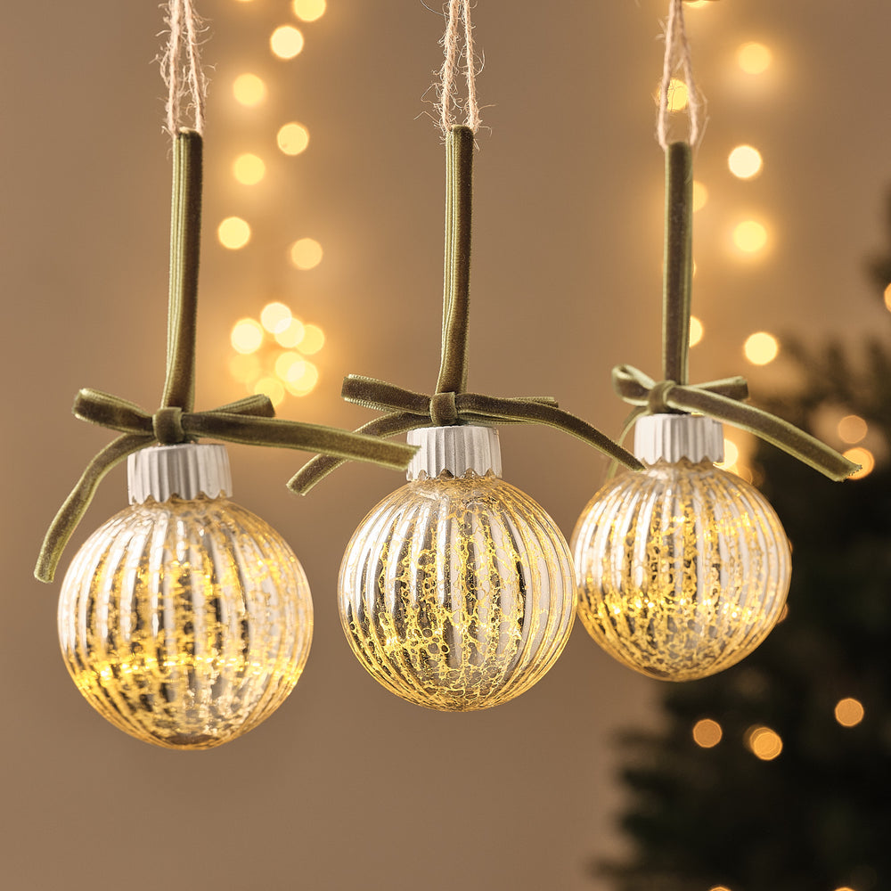 Drei LED-Weihnachtskugeln aus geriffeltem Glas mit grüner Schleife, warmweiß beleuchtet