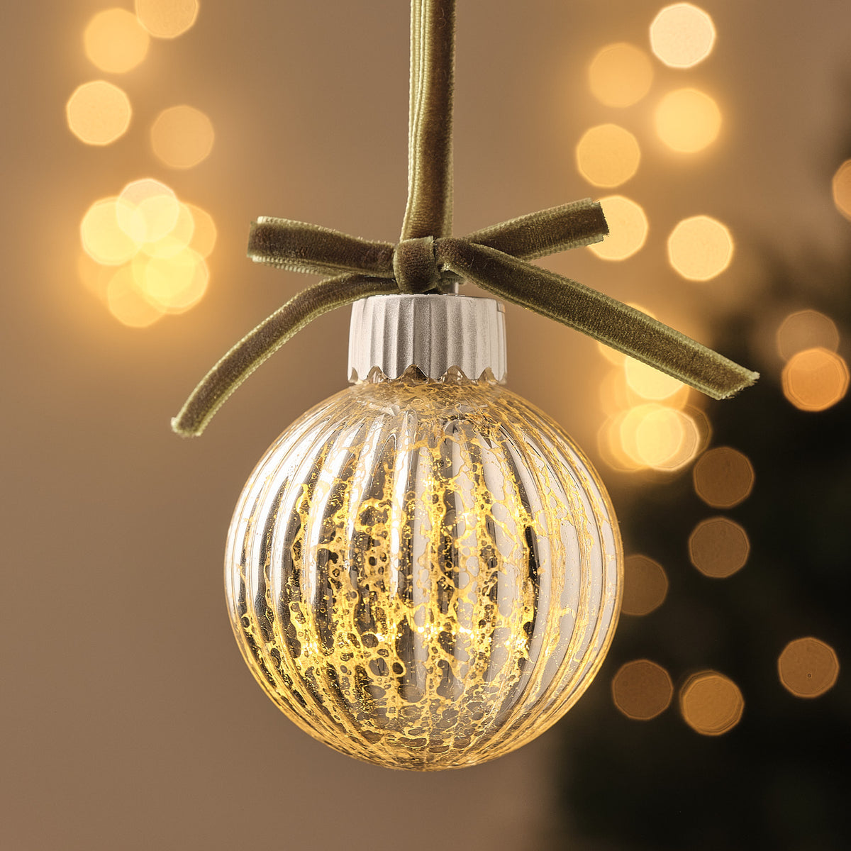 Nahaufnahme einer LED-Weihnachtskugel aus geriffeltem Glas mit grüner Schleife und warmweißem Licht