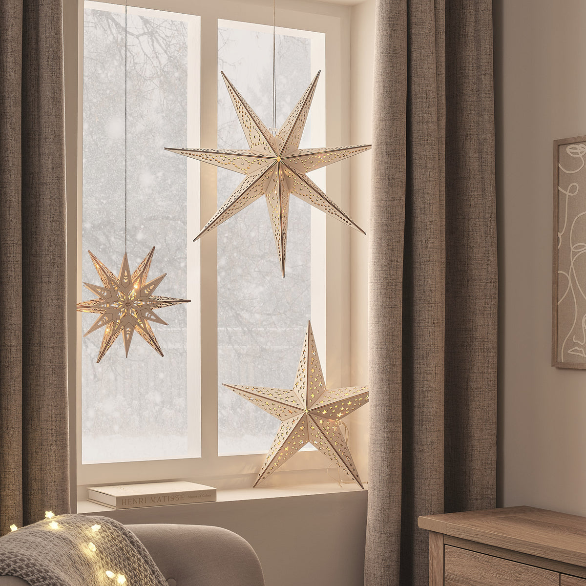 Goldene LED-Holzsterne mit 5, 6 und 7 Zacken hängen dekorativ vor einem Fenster mit Vorhängen