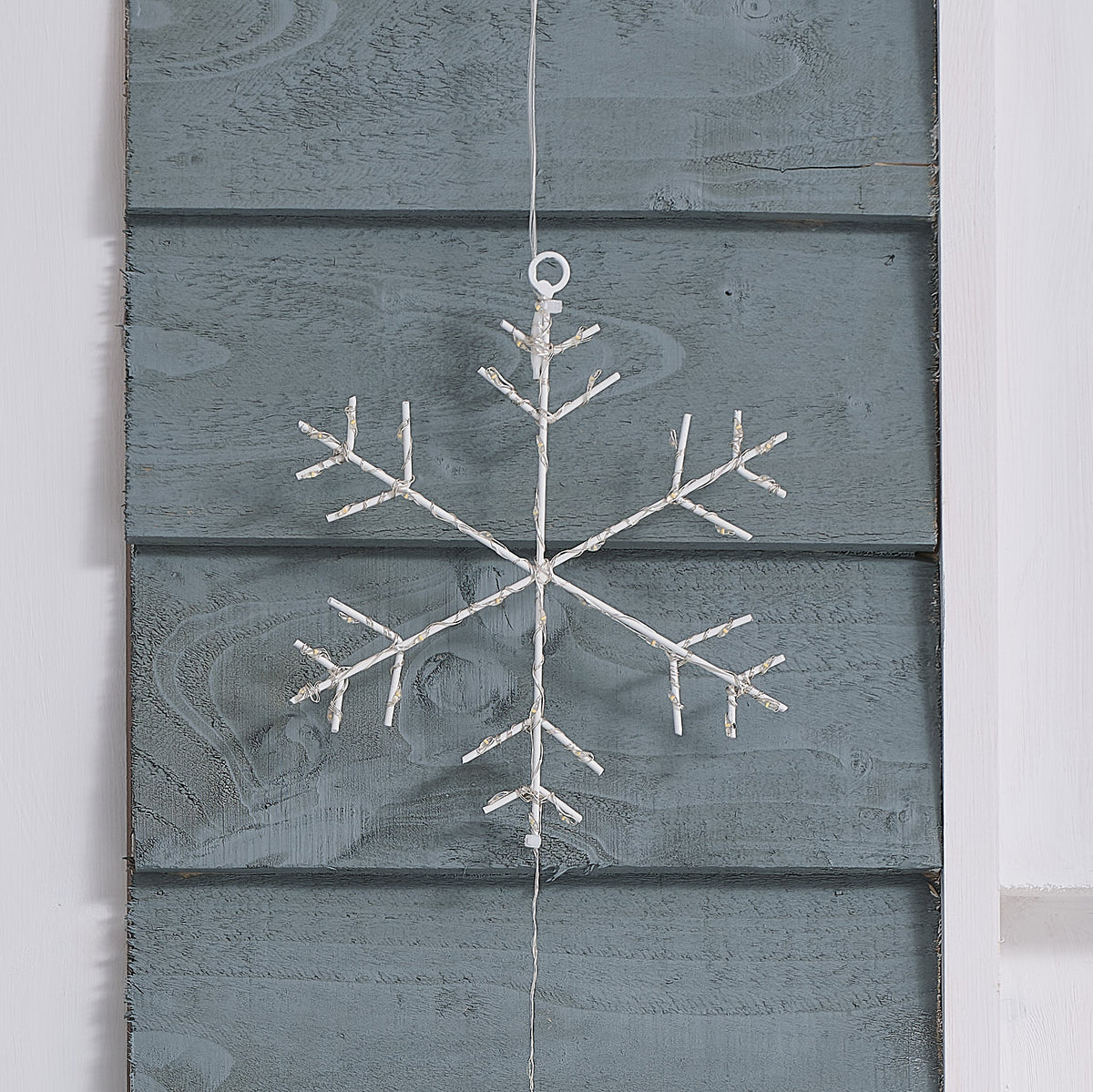 Detailaufnahme einer unbeleuchteten weißen LED-Schneeflocke an grauer Holzfassade