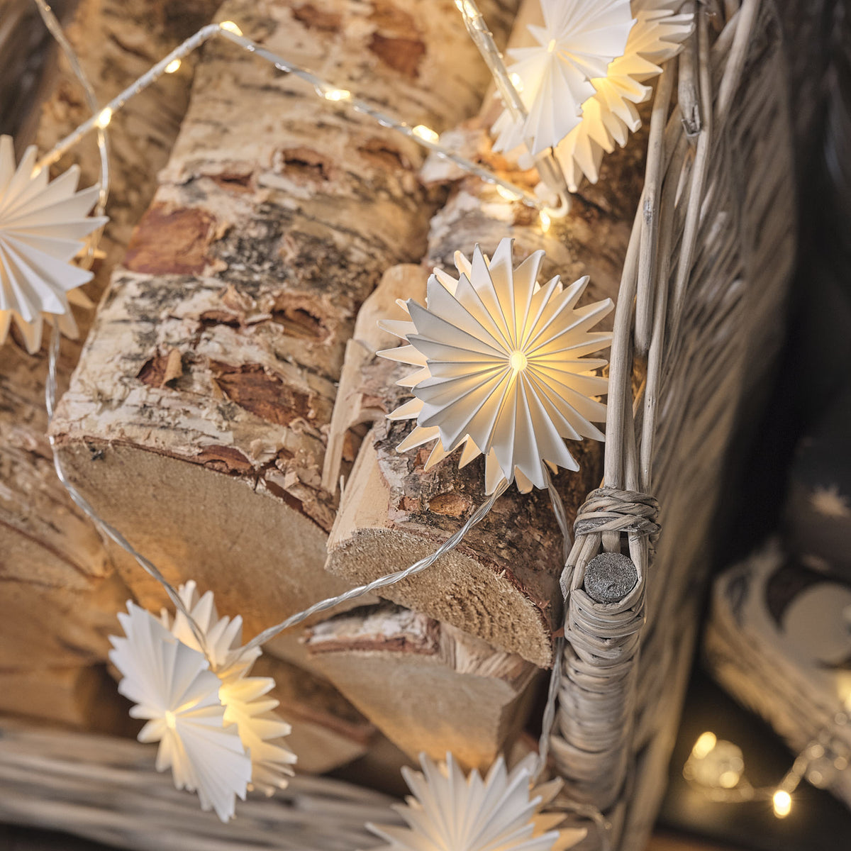 LED-Lichterkette mit Papier-Schneeflocken dekorativ auf Holzstämmen drapiert