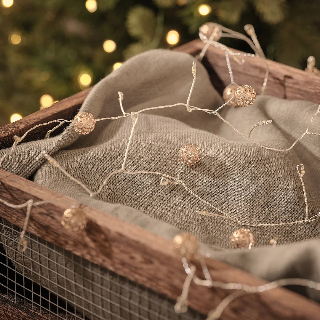 Festliche LED-Lichterkette mit warmweißen Leuchtperlen und cremefarbenen Organza-Schleifendekorationen vor dunklem Bokeh-Hintergrund mit unscharfen Lichtern, arrangiert auf Textil-Untergrund – elegante Lichterkette mit atmosphärischer Weihnachtsstimmung für Fenster, Kamine und gehobene Indoor-Dekoration.